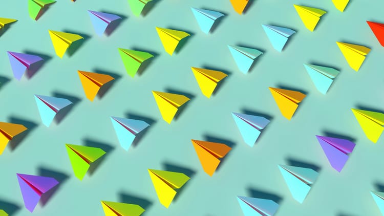 A fleet of paper aeroplanes of different colours, all pointing in the same direction