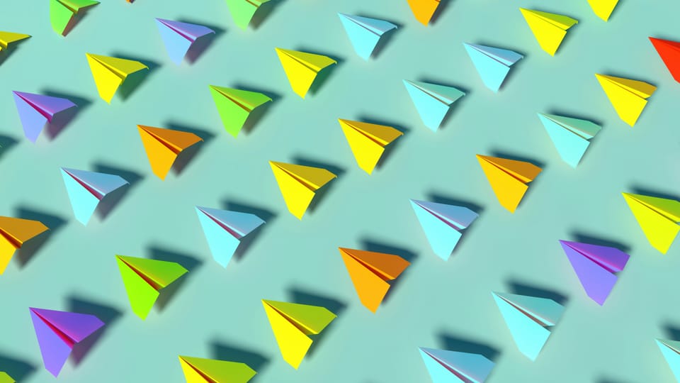 A fleet of paper aeroplanes of different colours, all pointing in the same direction